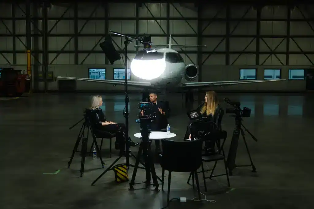 Professional film interview setup inside an airplane hangar with crew members, cameras, and lighting equipment.