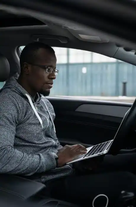 A man working on a laptop inside a car, focusing on work or browsing, representing mobile productivity and tech-savvy lifestyle.