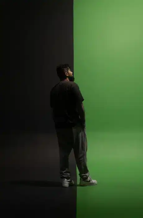 Man standing between dark and green background, creative photo, modern art, casual clothing, contemporary photography, visual contrast, fashion, and self-expression.