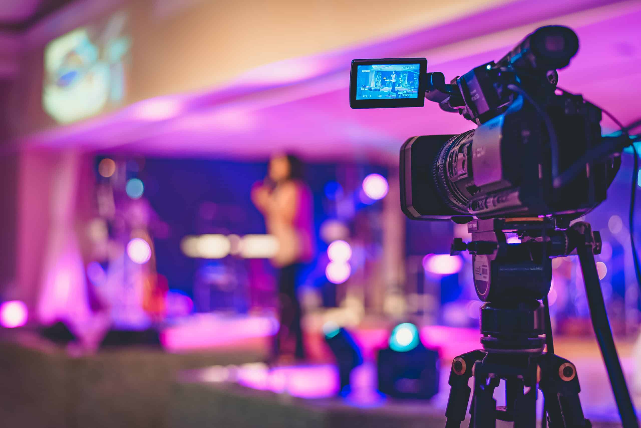 Camera filming a live event or performance with colorful stage lighting, creating a vibrant and dynamic atmosphere for video production and media coverage.