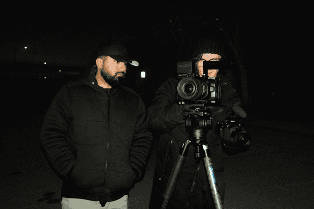 Unprofessional videographer filming at night with professional camera equipment and crew in dark outdoor setting for cinematic or media production.