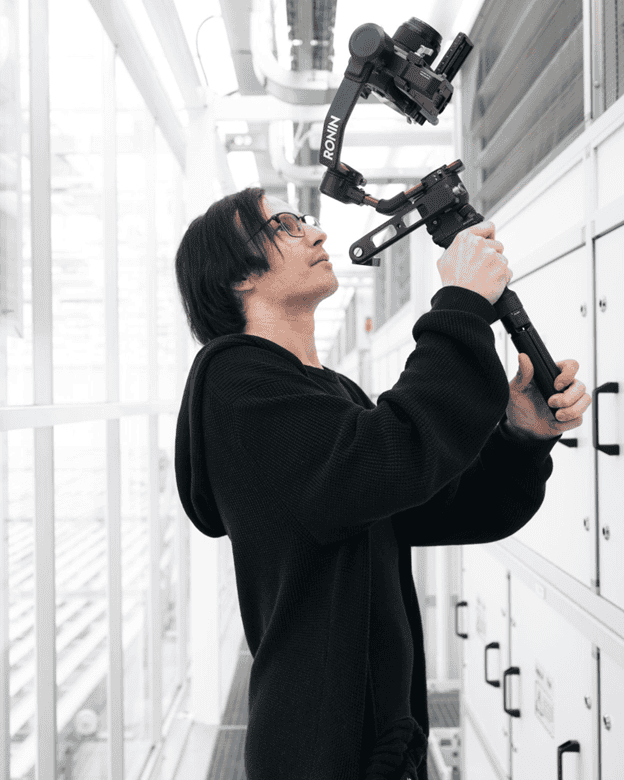 Drone camera operator at tech facility, professional videography, behind-the-scenes of drone filming, modern industrial environment, high-tech video equipment, capturing aerial footage.