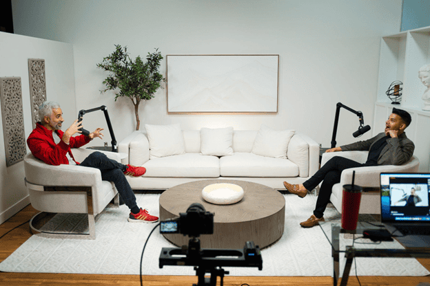 Q Filmz Media interview setup with two hosts recording a show in a modern, well-lit studio featuring microphones, camera equipment, and comfortable seating for engaging conversations.