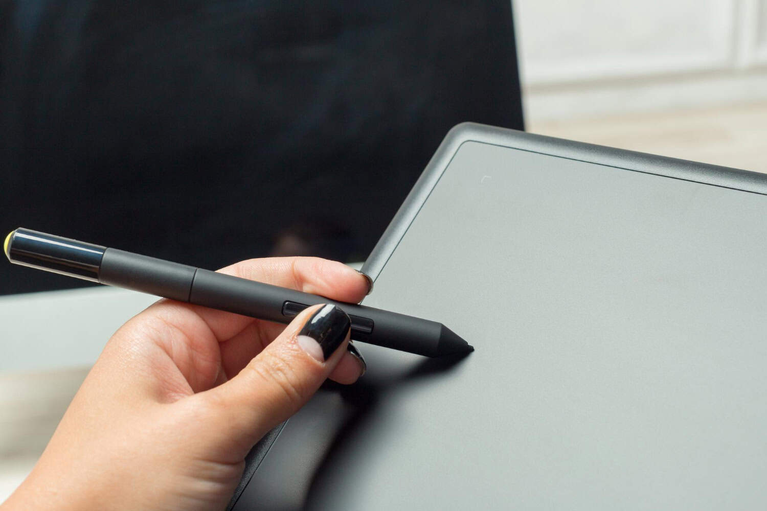 Close-up of a person using a stylus pen on a graphics tablet, illustrating digital art creation or graphic design work.