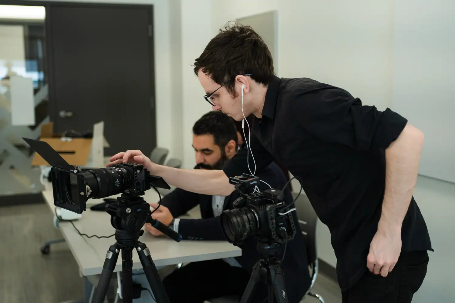Professional videographer operating a camera with crew member working on a laptop in a modern office setting, creating high-quality video content for Q Filmz Media.