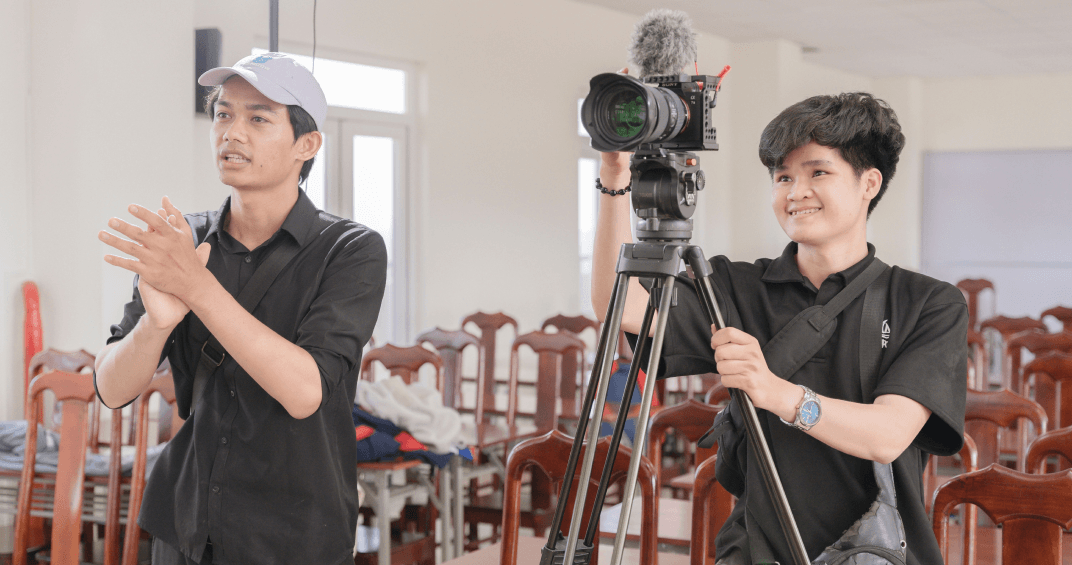 Two young men setting up a camera for an educational video in a classroom setting.