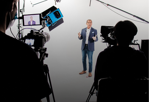 A man in a suit delivering a presentation in a professional video studio with cameras and lighting equipment.