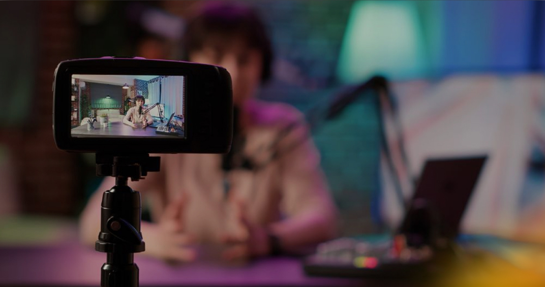 A professional camera records a testimonial video of a woman speaking in a modern studio setting, with a laptop and colorful background lights.
