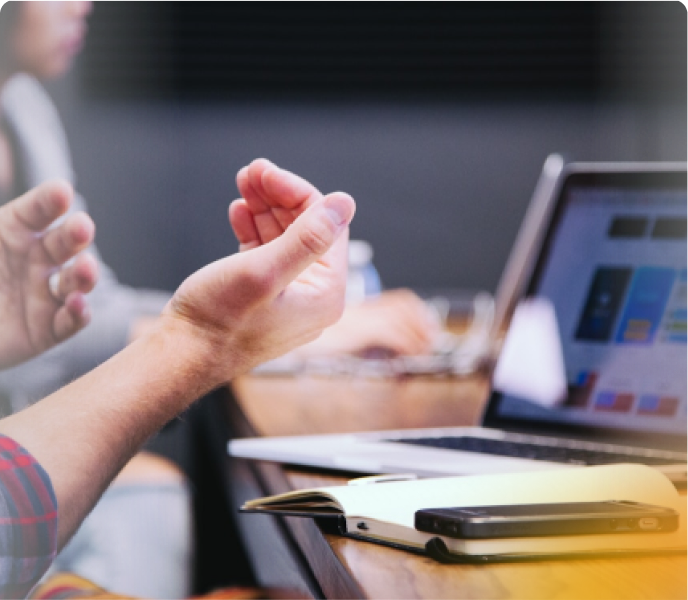 Close-up of a person gesturing during a business meeting with a laptop and documents on the table.