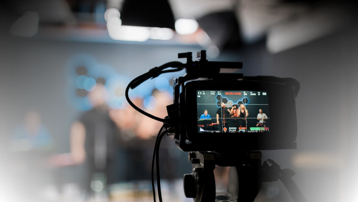Camera capturing a video shoot in a studio with blurred background and crew members.