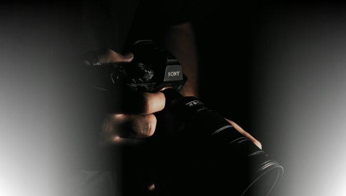 Close-up of a professional Sony camera being held by a photographer in a dark setting, emphasizing high-quality camera gear for media production.