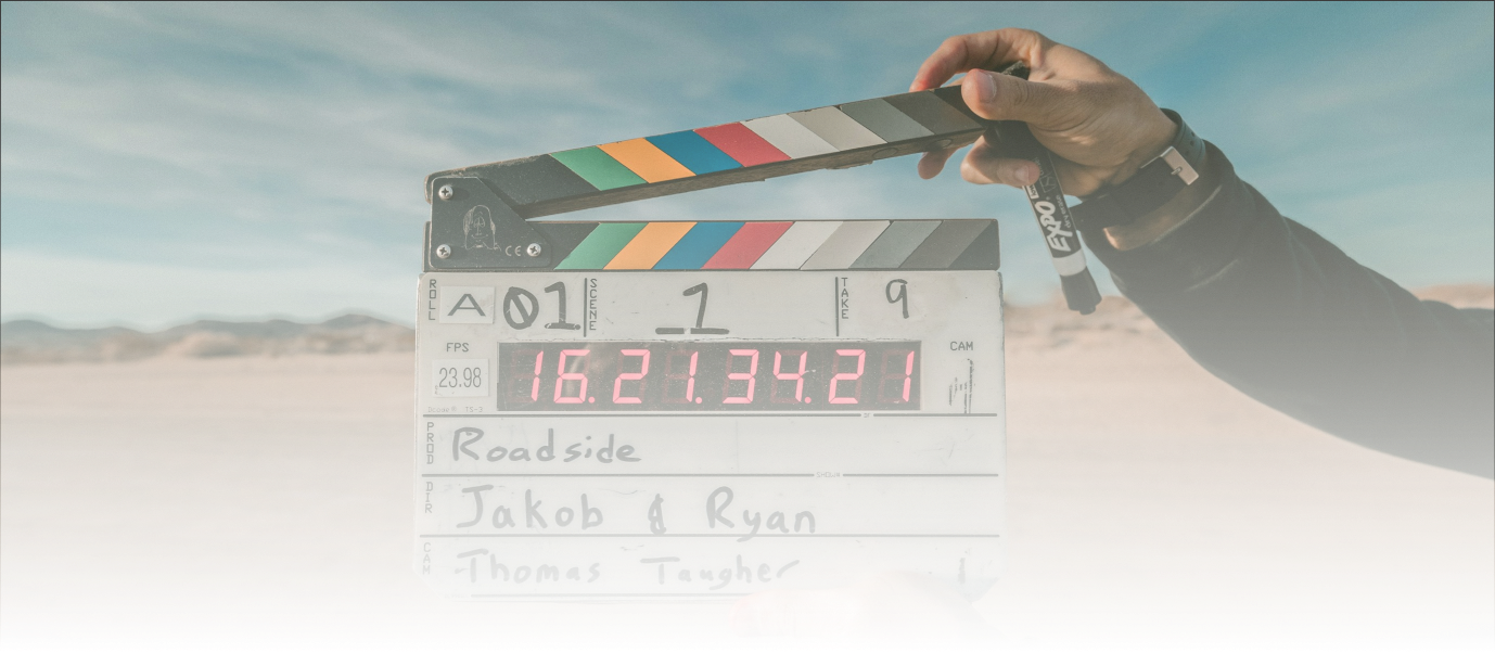 Close-up of a film clapperboard held by a person in a desert landscape, with mountains in the background, used for film production at Q Filmz Media.