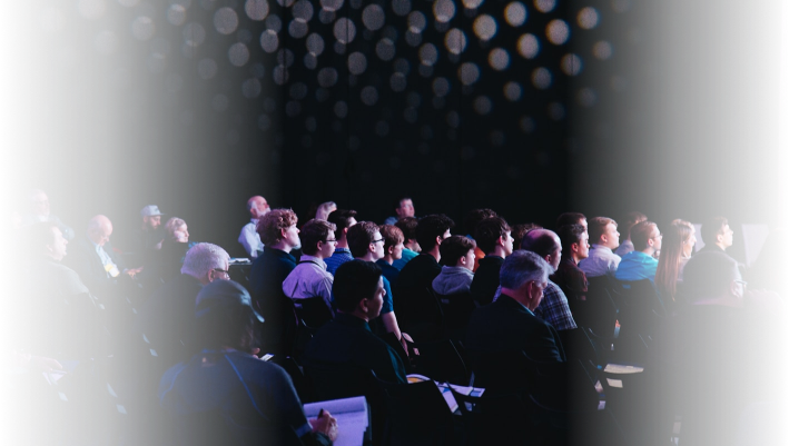 Audience attending a conference organized by Q Filmz Media, seated in a dark room with stage lighting and modern decor.