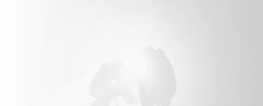 Two filmmakers working with a camera on a film set, backlit for dramatic effect, representing professional video production services.