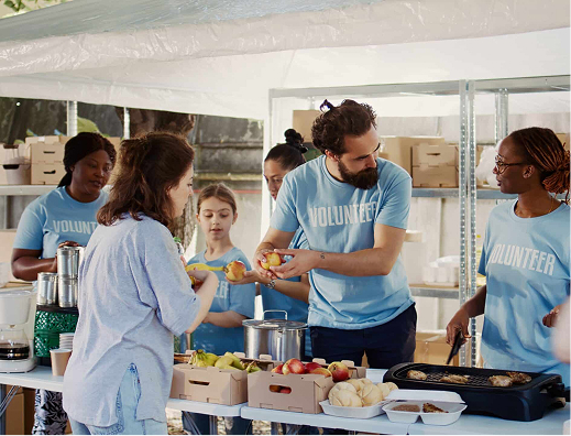Group of volunteers serving food at a community event, wearing blue volunteer shirts, under a white tent.