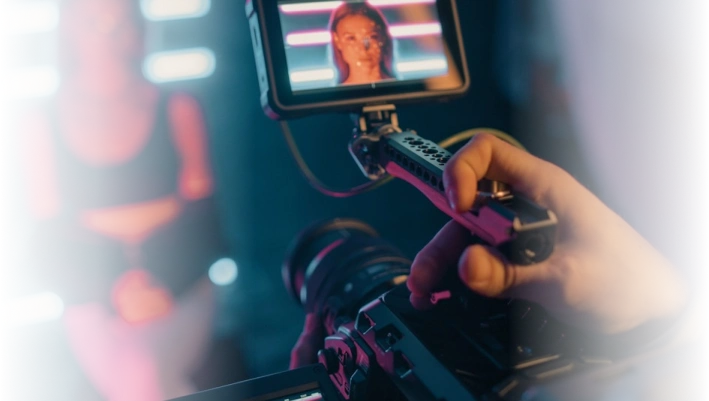 Close-up of a camera operator filming a woman on set with professional video equipment and monitor.