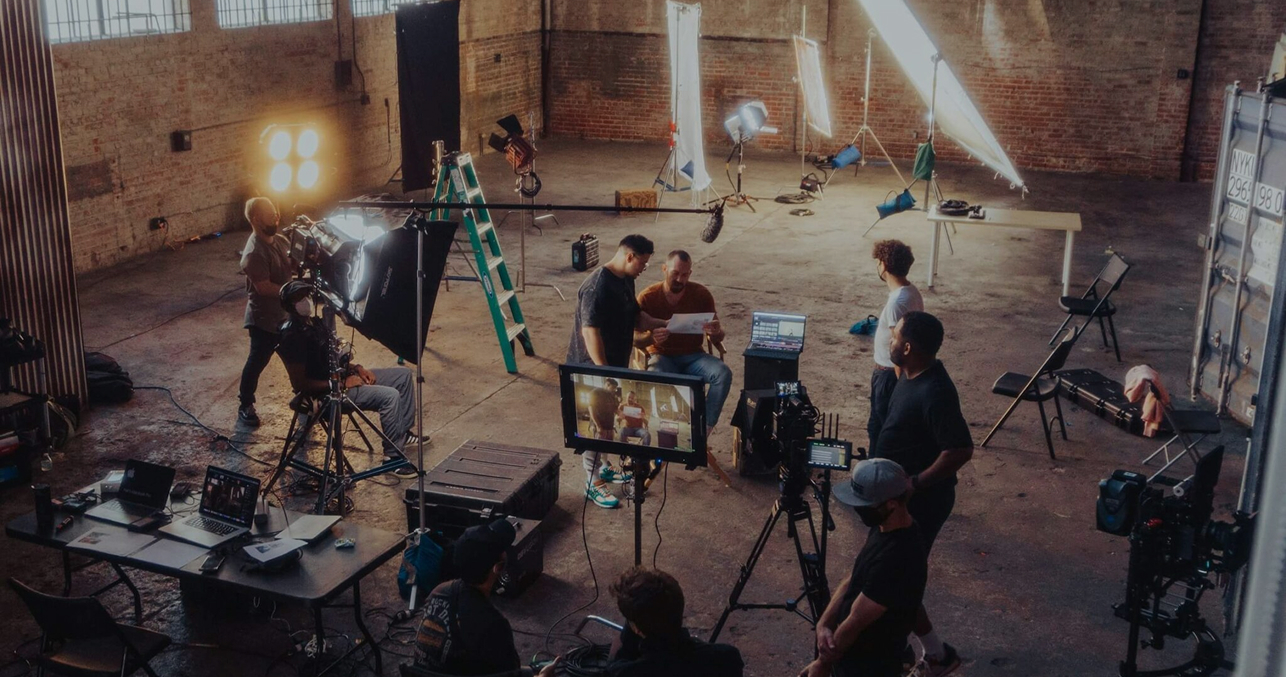 Film crew working on a video shoot in a spacious studio with professional lighting and camera equipment.