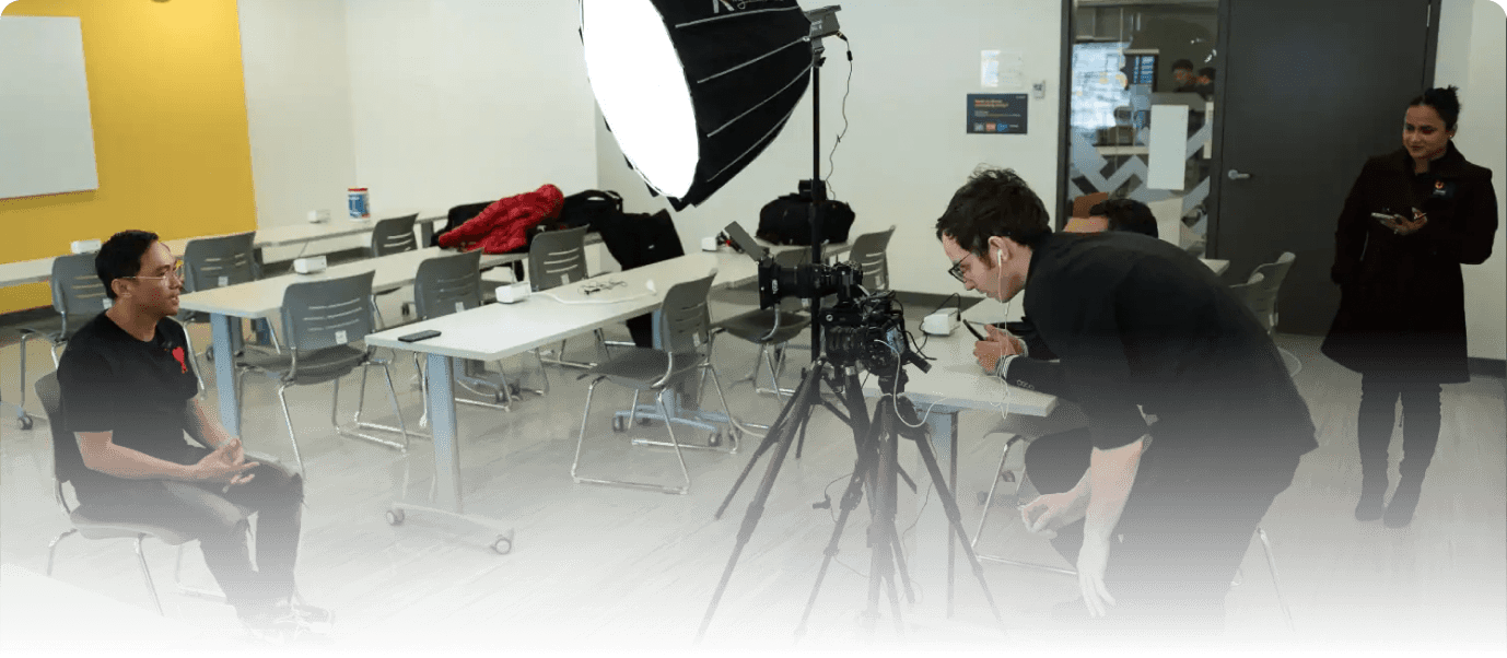 Behind the scenes of Q Filmz Media video shoot with camera, lighting, and crew in a modern office space.
