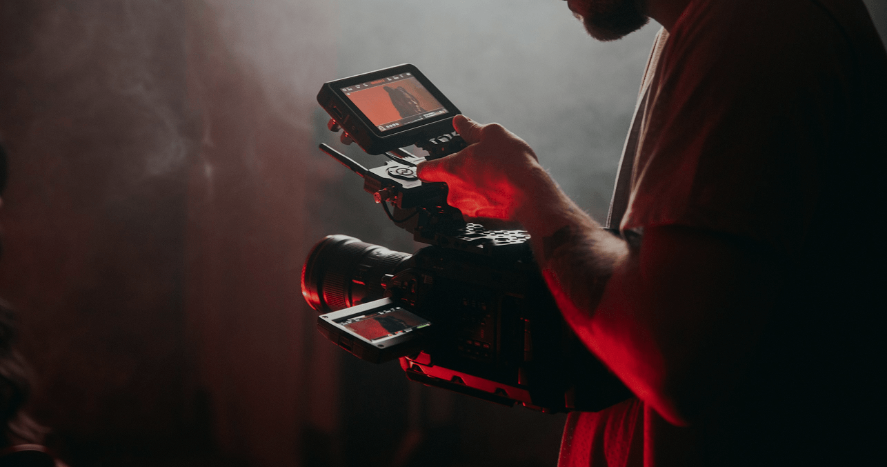 A filmmaker adjusting a professional video camera with a monitor, preparing for a shoot in a dimly lit environment.