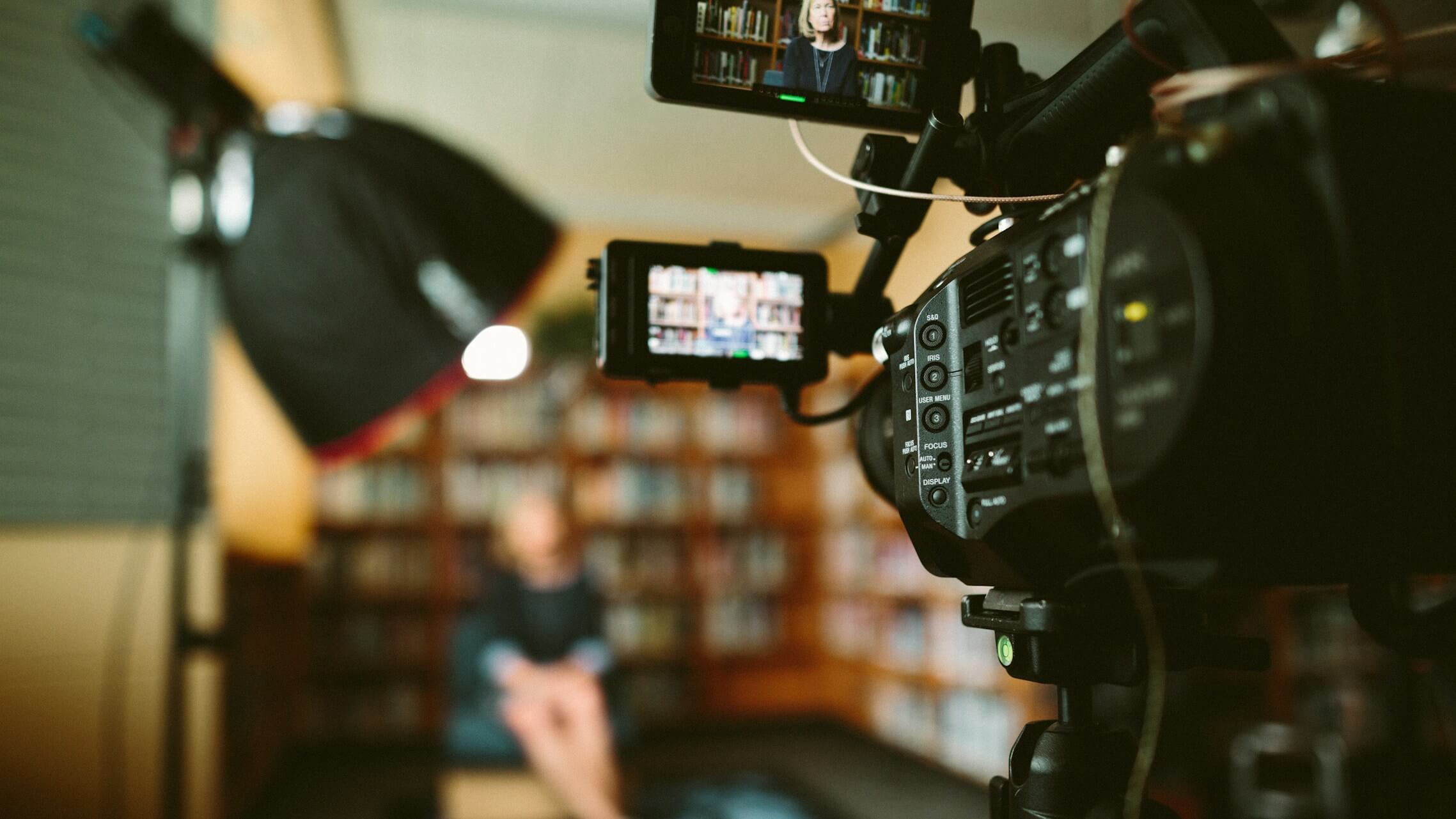 Professional video camera recording a person in a library setting for film production at Q Filmz Media.