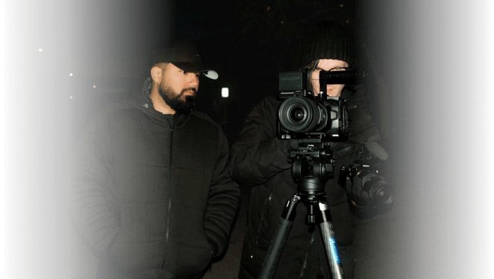 Two filmmakers working with professional camera equipment outdoors at night in Edmonton, capturing a video for advertising purposes.