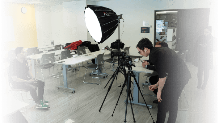 A video production crew filming a scene in a modern office space with professional lighting and camera equipment.