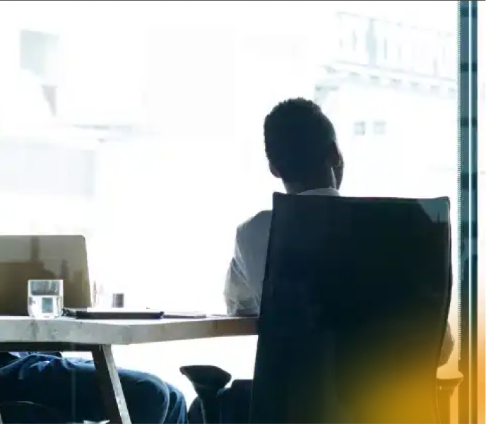 Professional man sitting at desk, gazing out of large window in modern office, contemplating work or future plans.