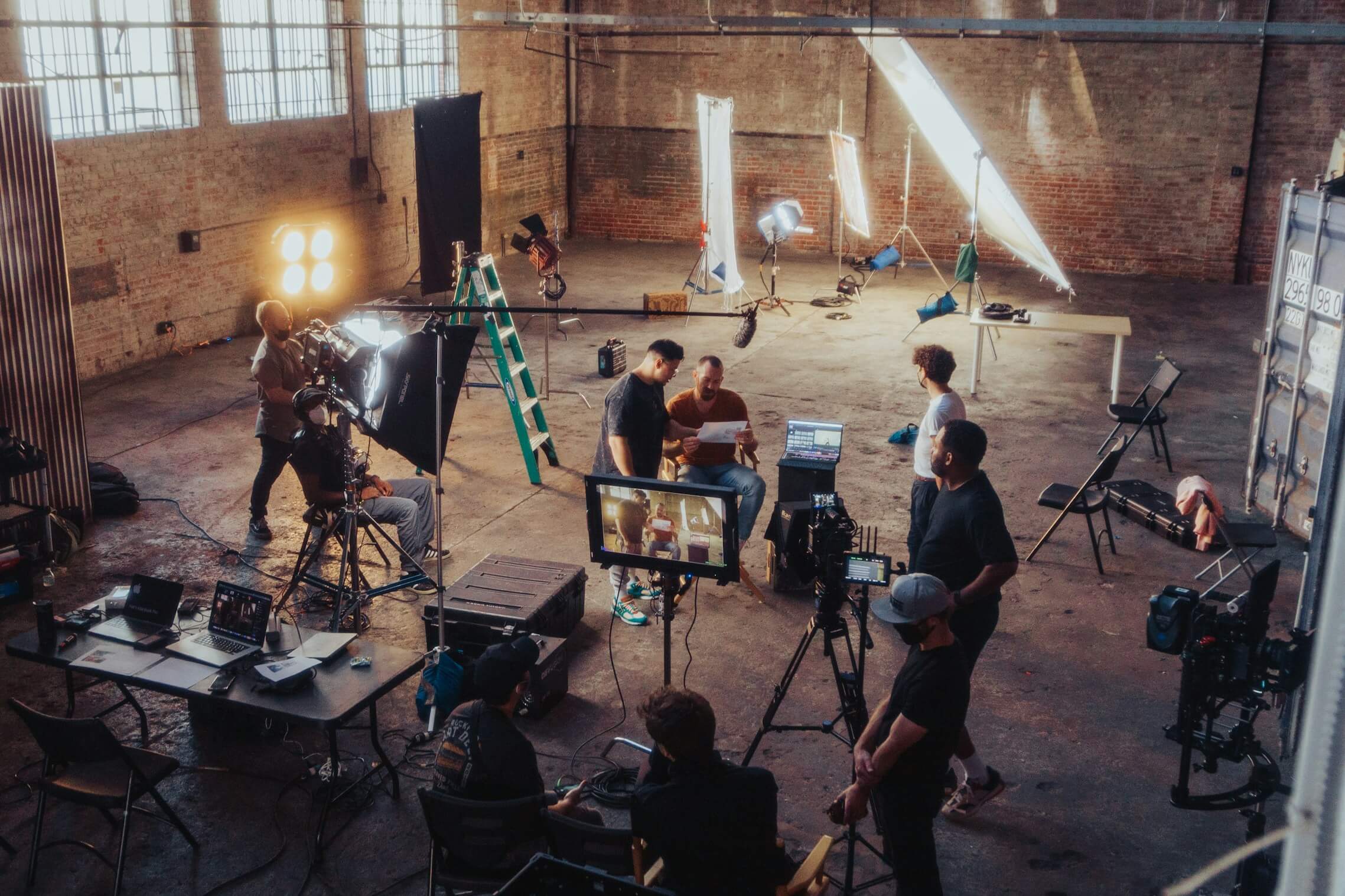 Behind the scenes of a professional film production with crew, cameras, and lighting equipment in an industrial studio setting.