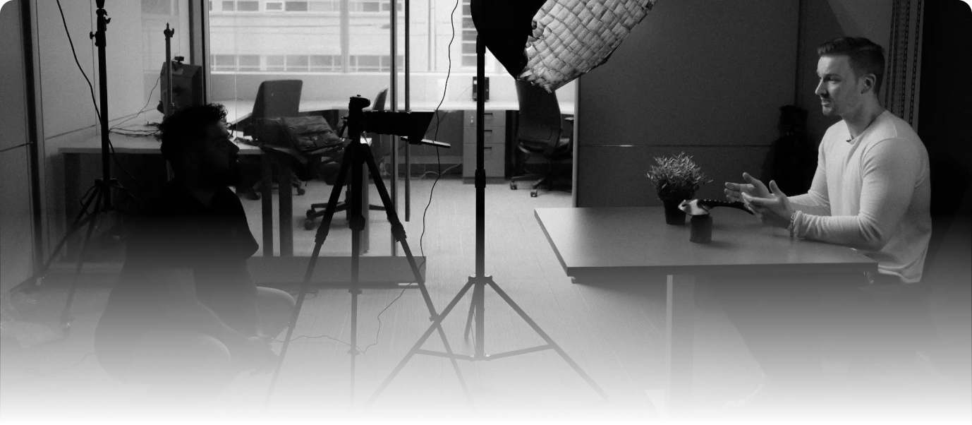Behind-the-scenes of a filmmaking interview with a camera operator and a speaker in a studio setting.